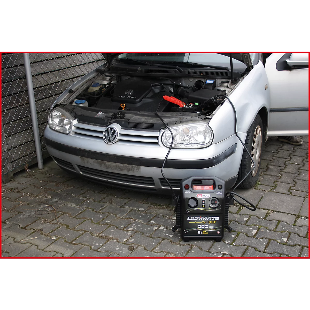 Ein silberner VW Golf mit geöffneter Motorhaube, Starthilfegerät angeschlossen. Darunter, ein schwarzes Ultimate-Gerät.